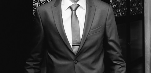 Groom is wearing the blue wedding suit. Stylish man is holding his tie in hands. Celebration day ceremony. Wedding fashion details. Black and white.