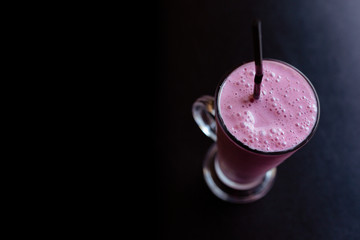 Refreshing drink-raspberry milkshake in a tall glass with a tube on a black background.