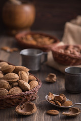 Rustic still life of almonds in the wicker plate on the dark rustic wooden background close up side view.