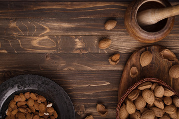 Flat lay of almonds in black plate with other accessories on brown wooden background top view 2