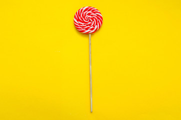 lollipop, a beautiful red and white striped round lollipop on a yellow background