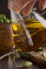 Extra virgin olive oil in glass bottle in the hand with olives on rustic background. low key