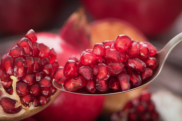 Spoon with pomegranate seeds on fresh ripe pomegranates background 2