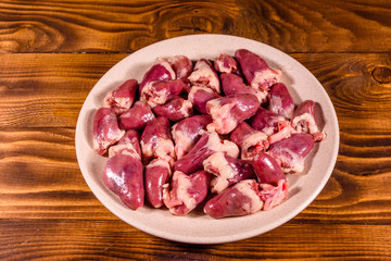 Ceramic plate with raw chicken hearts on wooden table