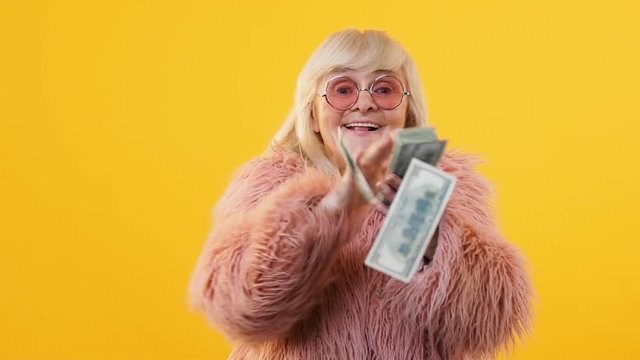 Excited aged lady throwing dollar bills around, lottery win financial investment