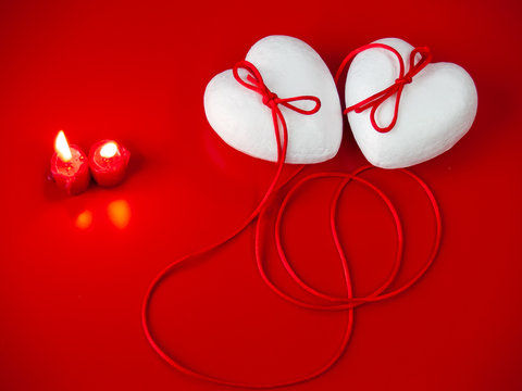 Concept of love Two poliespan hearts joined with a red thread that symbolizes the legend of the red thread and two red lit candles
