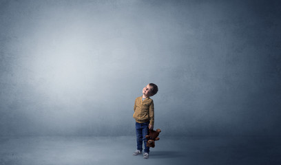 Little waggish kid staying alone in a big empty room with his plush
