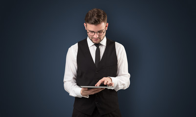 Handsome spectacled businessman holding a tablet with dark background
