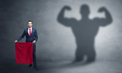 Businessman standing with red cloth on his hand and strong hero shadow on the background
