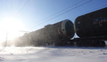 Freight train with oil tanks in motion. Snow dust flies from a passing train at high speed. Frosty sunny day. Winter. Russia.