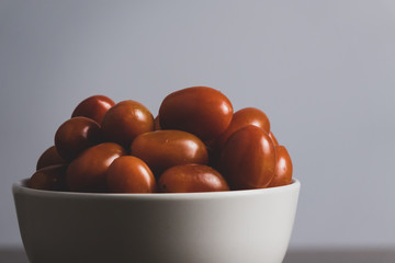 Tamatoes in white cup on wooden table.