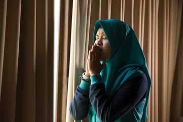 young sad and depressed Muslim woman in Islam traditional Hijab head scarf at home window feeling...
