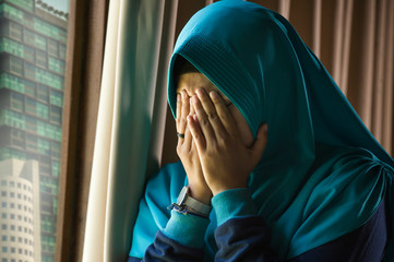 young sad and depressed Muslim woman in Islam traditional Hijab head scarf at home window feeling...