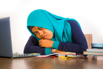 young stressed and overwhelmed Muslim student woman in Islam hijab head scarf  studying tired feeling overworked working with laptop computer and University books