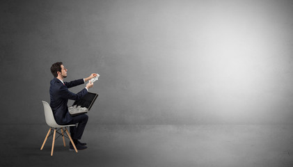 Businessman staying in an empty grey dark room with stuffs on his lap
