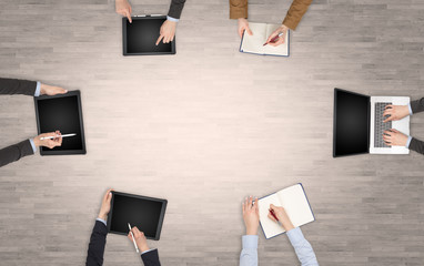 Group of people with devices in hands having desk discussion and making reports together on laptop,...