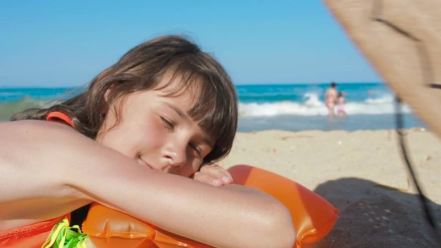 Wearing hat on child lying on sand. A cute little girl fell asleep in the sun, a parent puts a hat on her head.