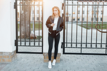 Beautiful young woman in a stylish black jacket in a white polo shirt in fashionable jeans in white...