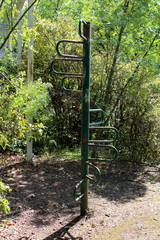 Fototapeta na wymiar Outdoor vintage public playground equipment metal partially rusted green climbing pole surrounded with overgrown forest vegetation on warm sunny day