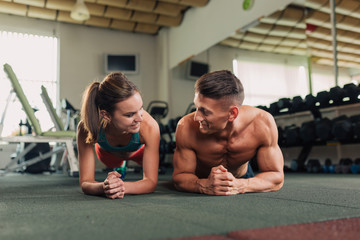 Young fit happy couple doing planking exercise in the gym