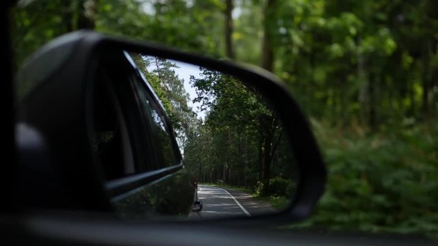 View out the rearview mirror as car drives on country road. 4K