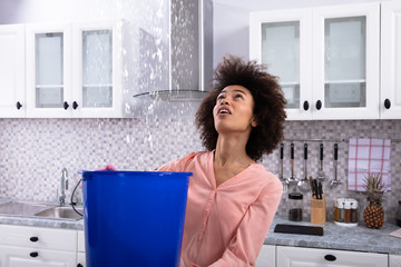 Woman Collecting Water Leaking From Ceiling In Bucket