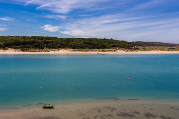 Long sandy beach in the village of Vila Nova de Milfontes, Alentejo region, Portugal. Small fishing boat in the foreground.