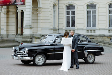 Happy luxury wedding couple kissing and embracing near retro with bouquet car in autumn
