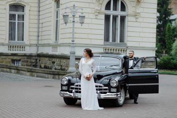 Fototapeta na wymiar Happy luxury wedding couple kissing and embracing near retro with bouquet car in autumn