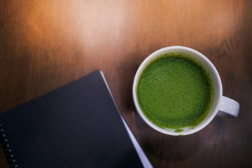 Cup of hot Green Tea Latte and Notebook on the Table in House or Cafe, Top View, Cropped and Closeup shot