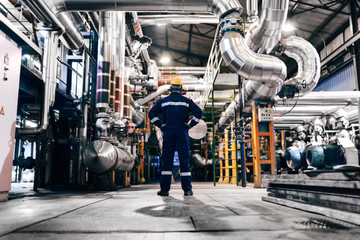 Caucasian worker in protective suit standing in heating plant with backs turned.