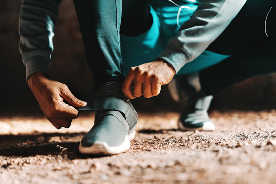 Close up of afro man putting on sneaker while kneeling in the brick factory.