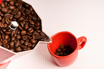 classical red moka pot filled with coffee beans pouring them into a red cup for espresso