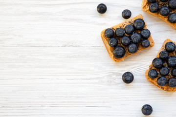 Vegan toasts with peanut butter, blueberries and chia seeds on a white wooden surface, top view. Healthy eating. Flat lay, from above. Space for text.