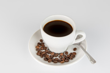White Cup of black coffee on a white background, with some beans on the saucer