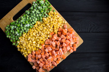 Frozen vegetables in the brown cutting board on the black wooden background.Top view.Copy...