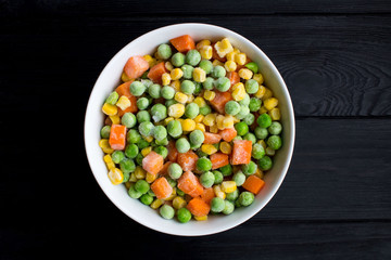 Frozen vegetables in the white bowl on the black wooden background.Top view.Copy space.Healthy food ingredients.