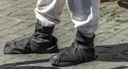 Medieval waistband shoes made of soft black leather stripes over a light grey linen trousers