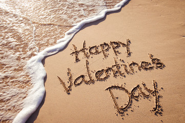 Happy Valentine's Day message handwritten in smooth sand copy space with foamy wave 