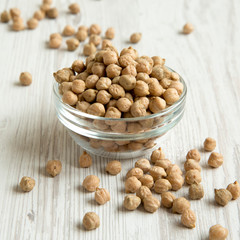 Full bowl of dried chickpeas on a white wooden table, side view. Close-up.