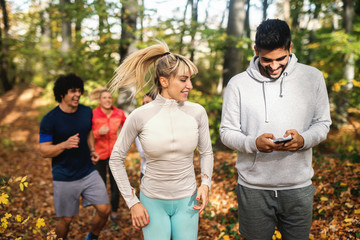 Man using smart phone while his friends running in the woods. Autumn season.