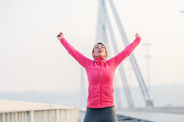 Obraz premium Gorgeous brunette lifting arms in the air and feeling free after running on the bridge. Winter time, healthy lifestyle concept.