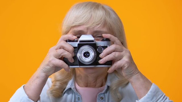 Smiling aged lady taking photo by old-style camera, retirement hobby, work