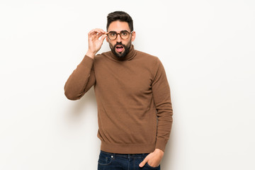 Handsome man over white wall with glasses and surprised
