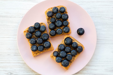Vegan toasts with peanut butter, blueberries and chia seeds on a pink plate over white wooden background, overhead view. Flat lay, from above.