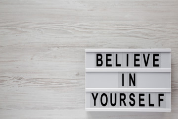 'Believe in yourself' words on lightbox on a white wooden surface, top view. From above, flat lay, overhead. Copy space.