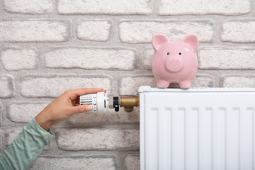 Person Adjusting Thermostat With Piggy Bank