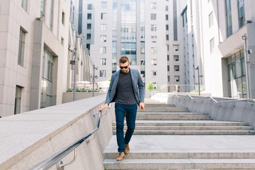 Full-length photo of  man in sunglasses walking on concrete stairs on  office building background....