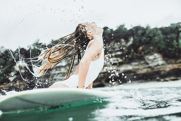 Beautiful woman on a surfboard in the ocean. Surf in the rain. wet hair and spray. Girl  in a white...