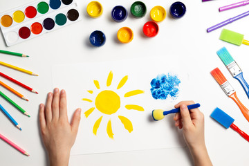 Kid hands painting at the table with art supplies, top view